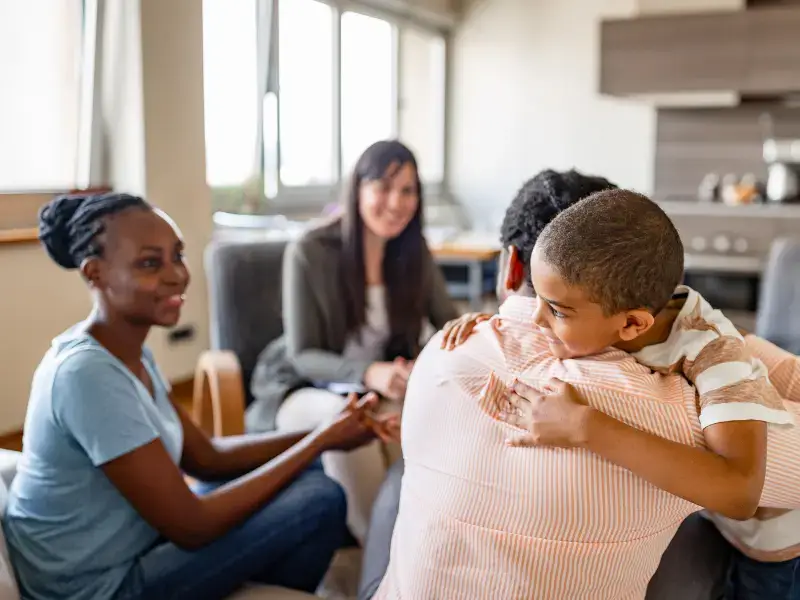 A therapist in the background with a family of three, looking happy, smiling and the kid hugging his dad.