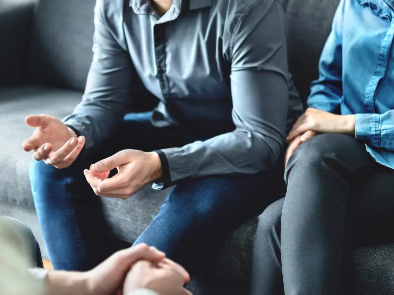 A couple sitting on a couch, talking to a therapist during couple counselling