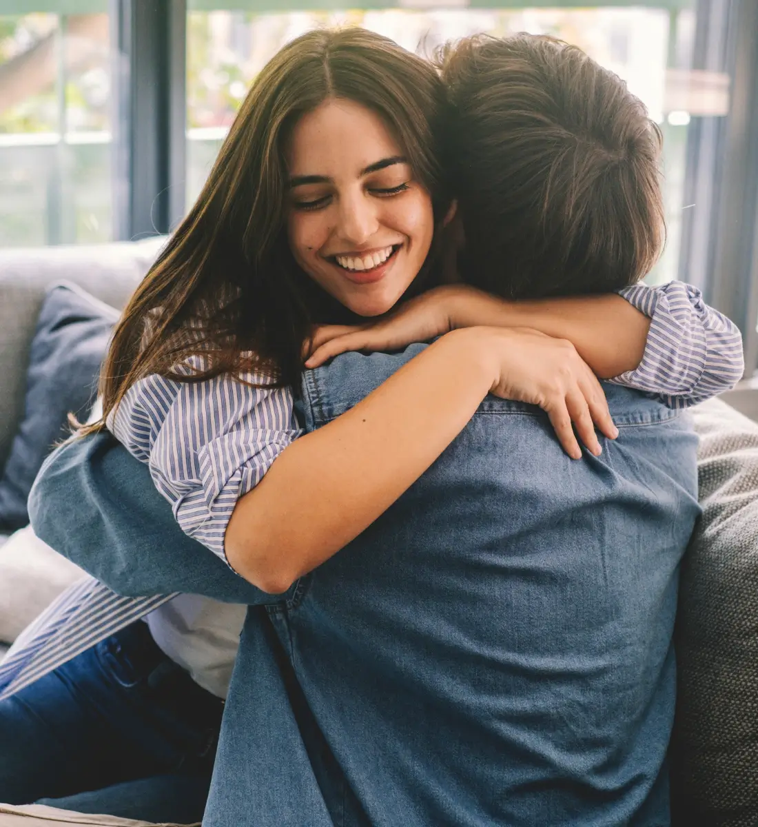 A couple hugging each other. The woman, facing us, is smiling and looking happy.