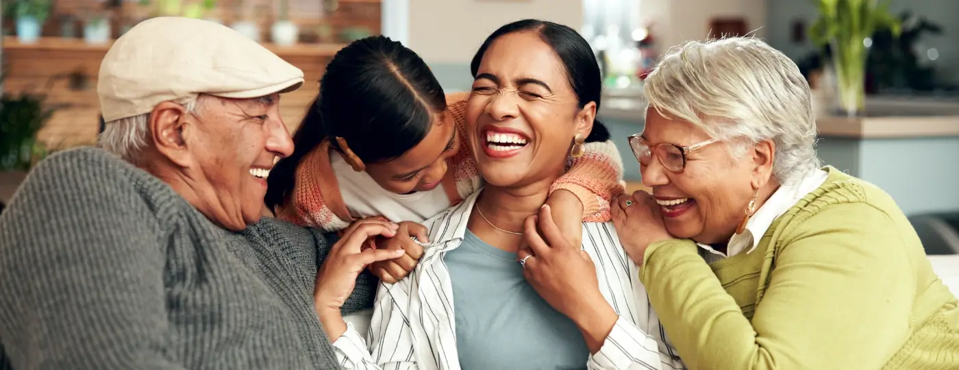 A family - the two grand-parents, the daughter and their grand-daughter, hugging each other and laughing, looking happy