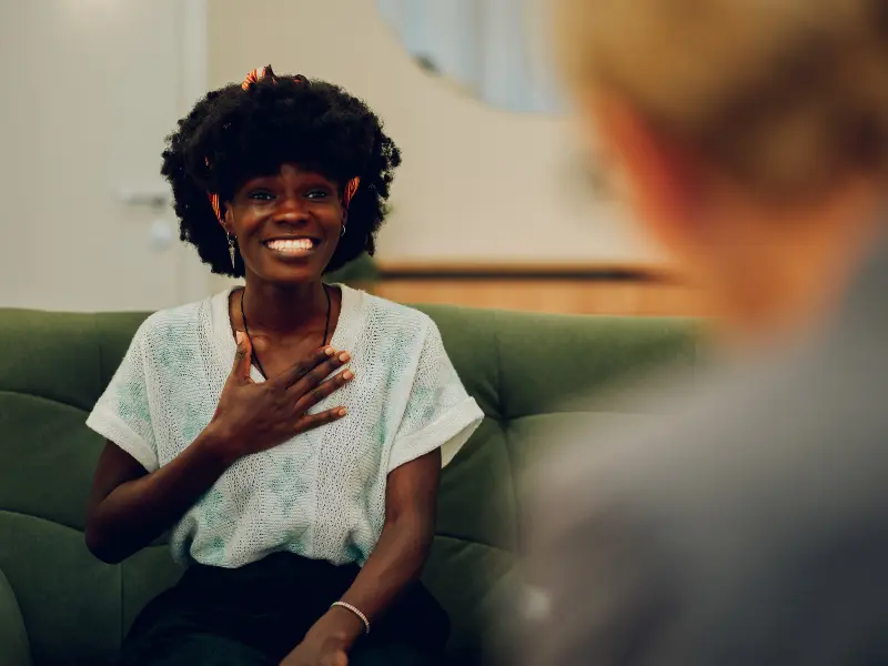 A woman talking to a therapist, smiling and looking happy with a hand on her chest, feeling relieved