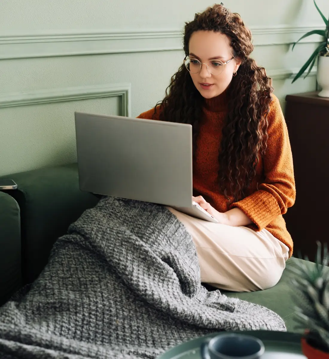 Une jeune femme assise confortablement sur son canapé avec son ordinateur portable sur les genoux, en train de faire une thérapie en ligne.