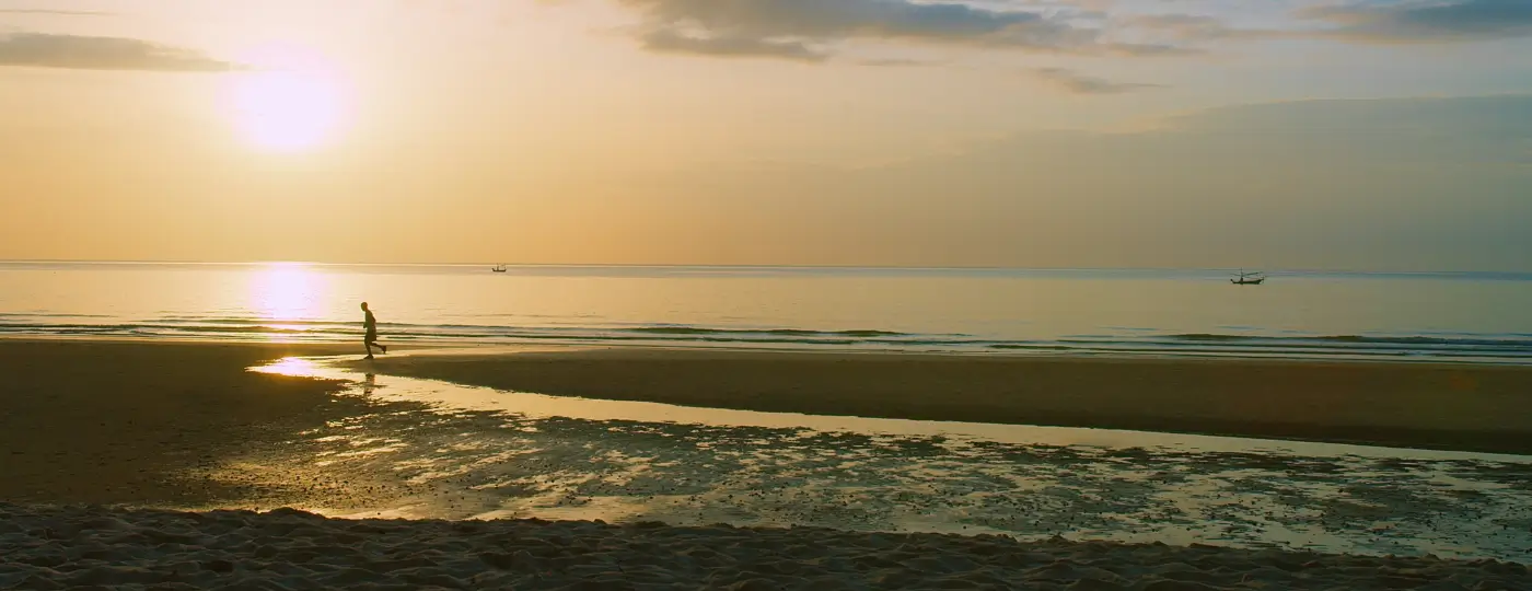 A sunset on a beach, looking peaceful, with a person walking along the beach.