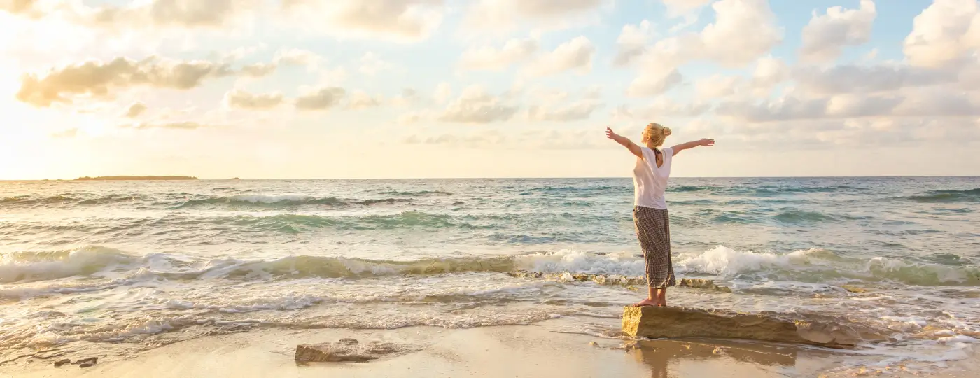 A woman standing in front of the ocean with her arms extended, looking free and relaxed