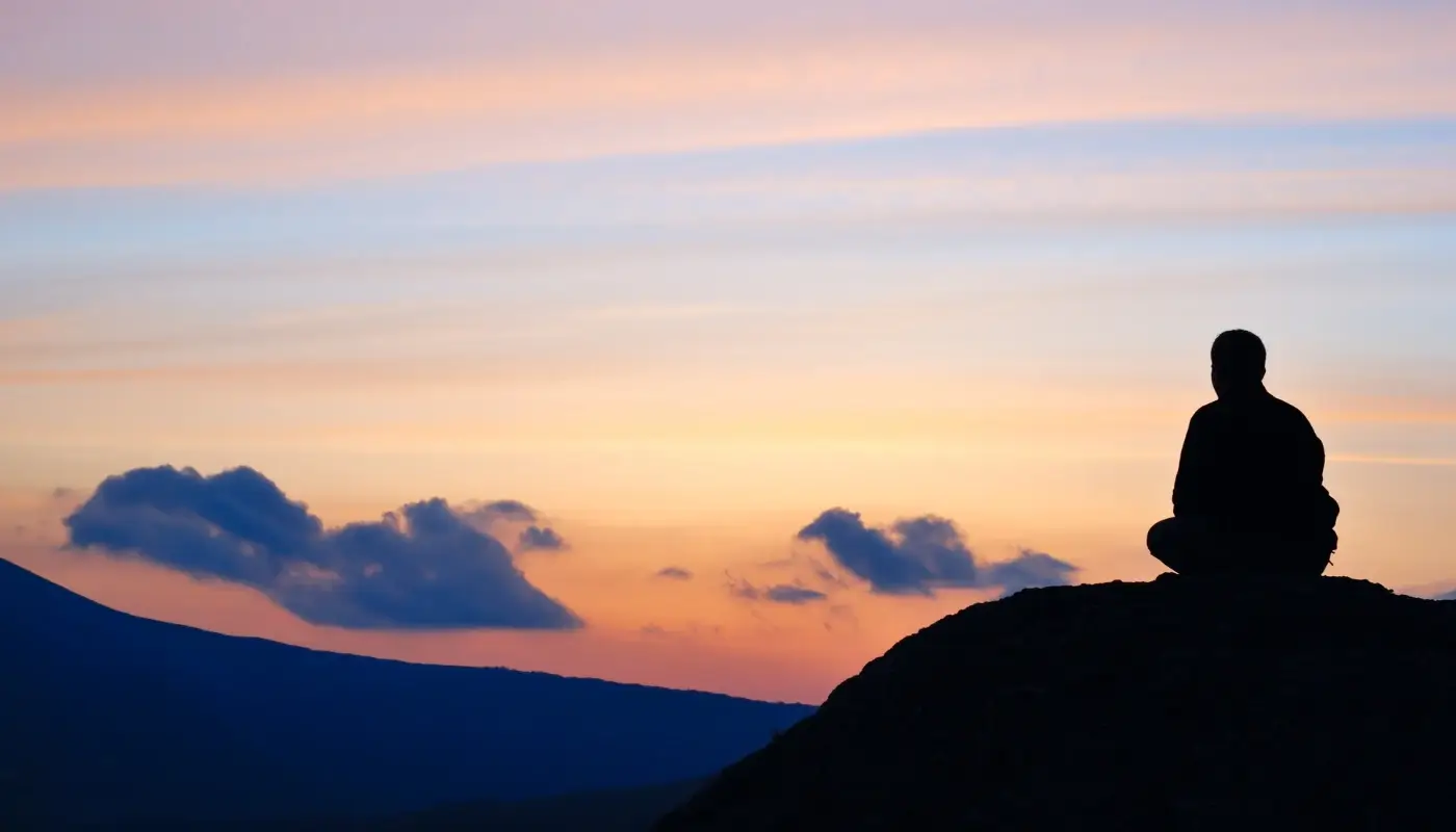 A man on top of a mountain, facing the sunset