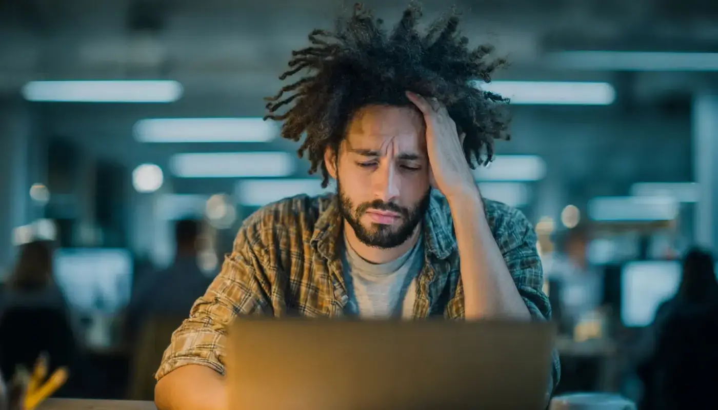A man in front of his computer, looking tired and anxious.